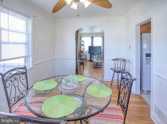 dining space with light wood-type flooring, visible vents, ornamental molding, a ceiling fan, and arched walkways