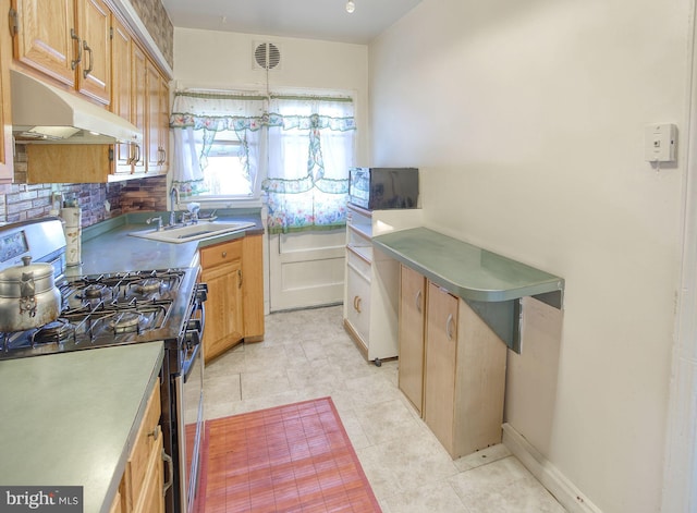 kitchen with under cabinet range hood, a sink, light tile patterned flooring, decorative backsplash, and stainless steel gas range