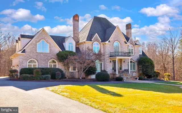 view of front facade featuring brick siding, a chimney, a front yard, and a balcony