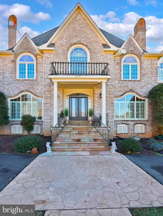 property entrance with a balcony, a chimney, french doors, central air condition unit, and brick siding