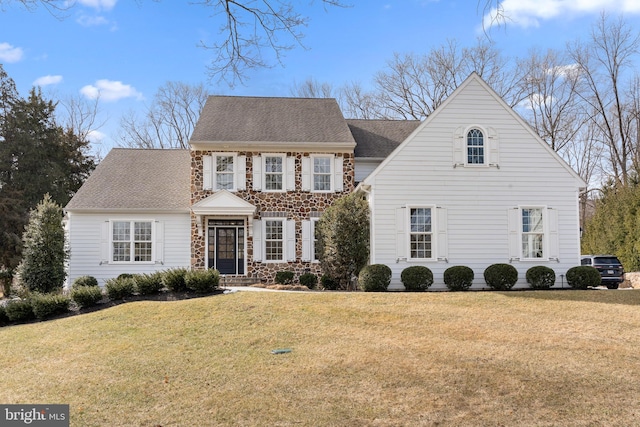 colonial house with stone siding, roof with shingles, and a front yard