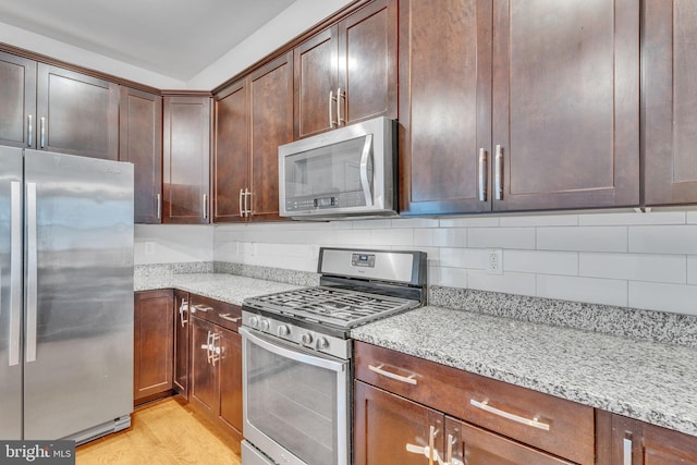 kitchen with appliances with stainless steel finishes, backsplash, light wood-style flooring, and light stone countertops