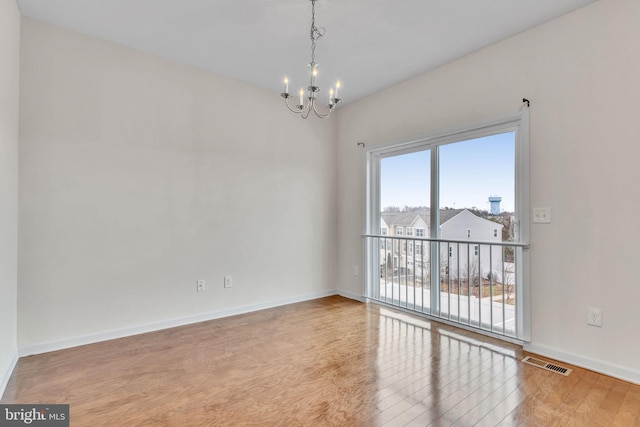 spare room with visible vents, a notable chandelier, baseboards, and wood finished floors