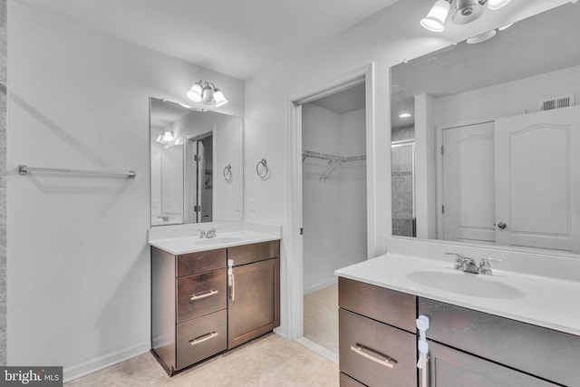 full bath with visible vents, two vanities, a sink, and tiled shower