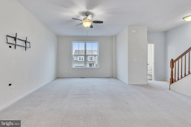 carpeted spare room featuring stairs, a ceiling fan, and baseboards