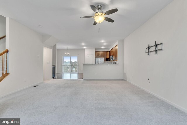 unfurnished living room featuring ceiling fan with notable chandelier, stairway, baseboards, and light colored carpet