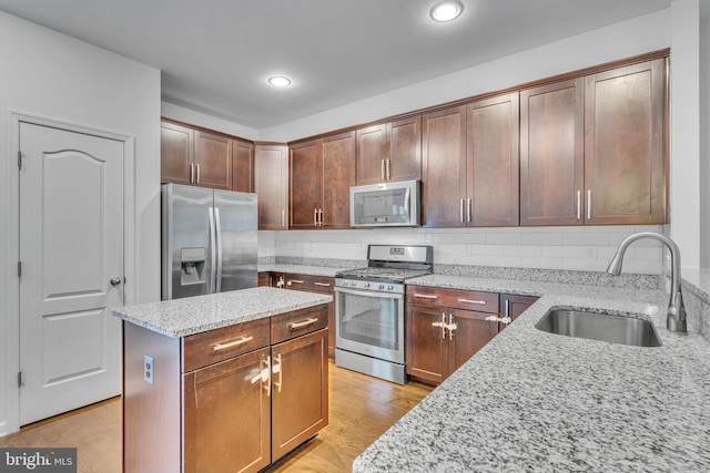 kitchen featuring light wood-style flooring, a sink, appliances with stainless steel finishes, light stone countertops, and tasteful backsplash