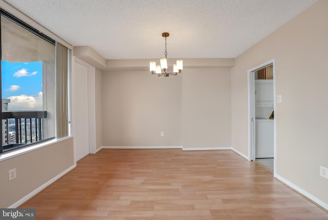 spare room featuring light wood-style flooring, a notable chandelier, baseboards, and a textured ceiling