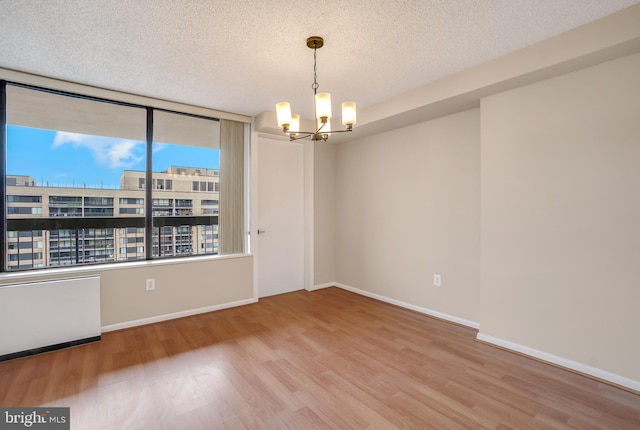 unfurnished room featuring baseboards, a textured ceiling, an inviting chandelier, and wood finished floors