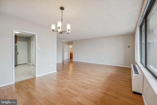 empty room with baseboards, radiator heating unit, light wood-style floors, a notable chandelier, and a textured ceiling