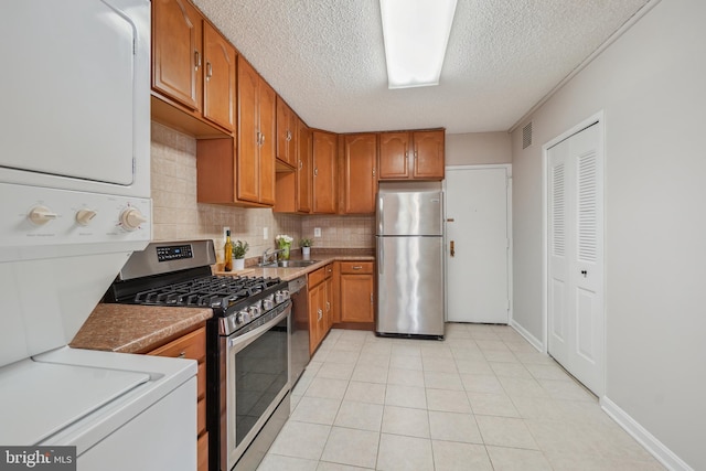 kitchen with brown cabinetry, stacked washer / drying machine, appliances with stainless steel finishes, and a sink