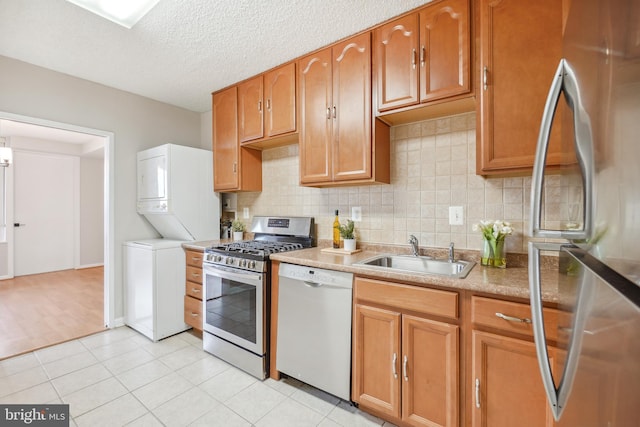 kitchen with a sink, stainless steel appliances, stacked washer / drying machine, a textured ceiling, and tasteful backsplash