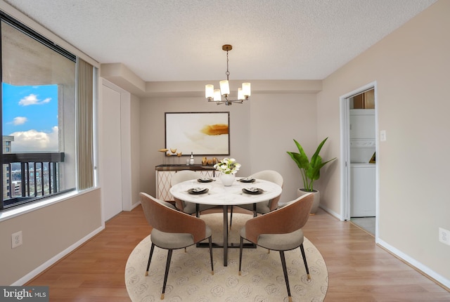 dining area featuring a notable chandelier, light wood-style flooring, a textured ceiling, and stacked washing maching and dryer