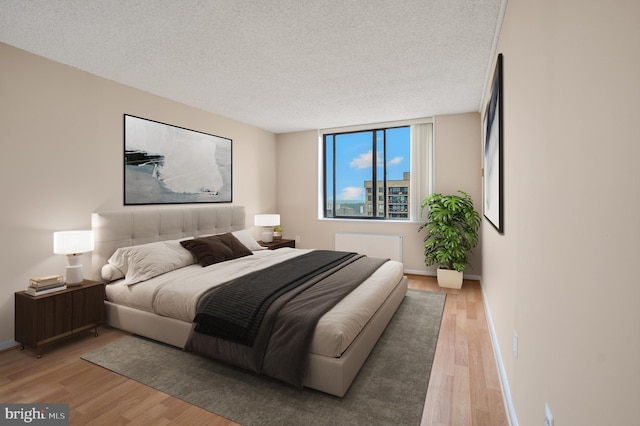 bedroom with a textured ceiling, light wood-type flooring, and baseboards