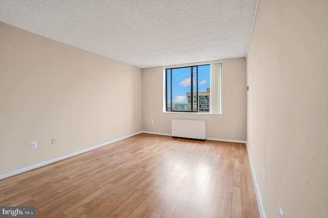 unfurnished room with light wood finished floors, a textured ceiling, radiator heating unit, and baseboards