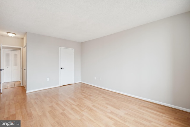 spare room featuring light wood-type flooring, baseboards, and a textured ceiling