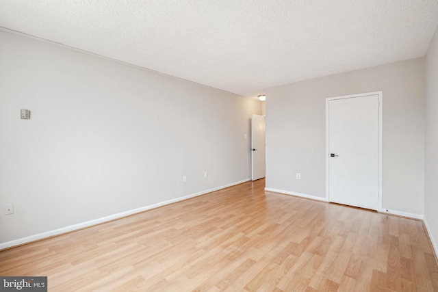 empty room with light wood-style flooring, a textured ceiling, and baseboards