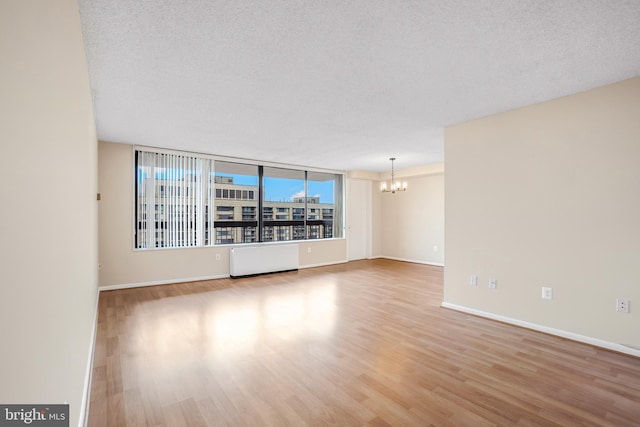 empty room featuring radiator, a textured ceiling, an inviting chandelier, and wood finished floors