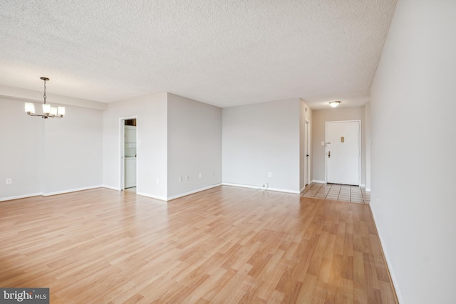 unfurnished room with a textured ceiling, baseboards, a notable chandelier, and light wood finished floors