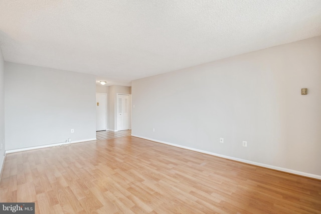 empty room with baseboards, light wood finished floors, and a textured ceiling