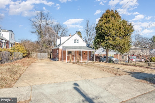 view of front facade featuring a porch, brick siding, fence, concrete driveway, and a chimney