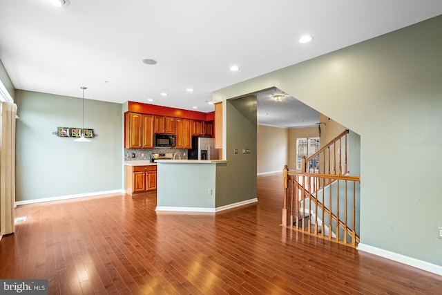 kitchen with black microwave, decorative backsplash, wood finished floors, and stainless steel fridge with ice dispenser