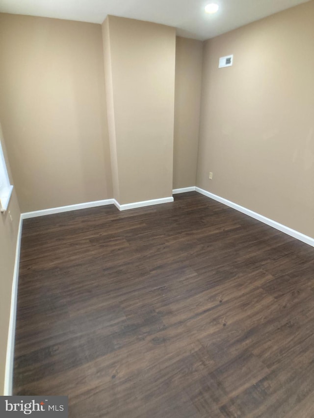 empty room featuring dark wood-style flooring, visible vents, and baseboards