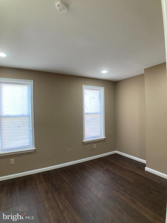 empty room with dark wood-type flooring, recessed lighting, and baseboards