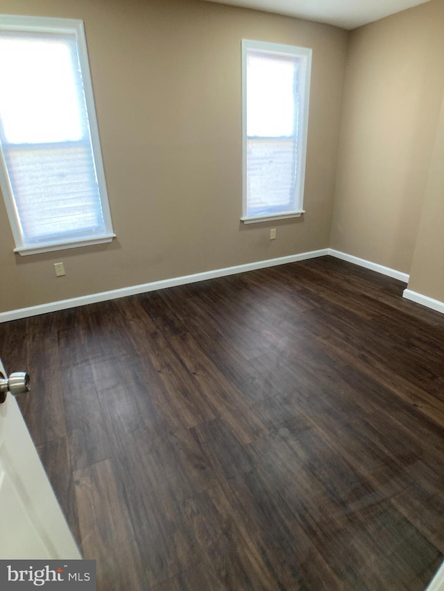 spare room with baseboards and dark wood finished floors