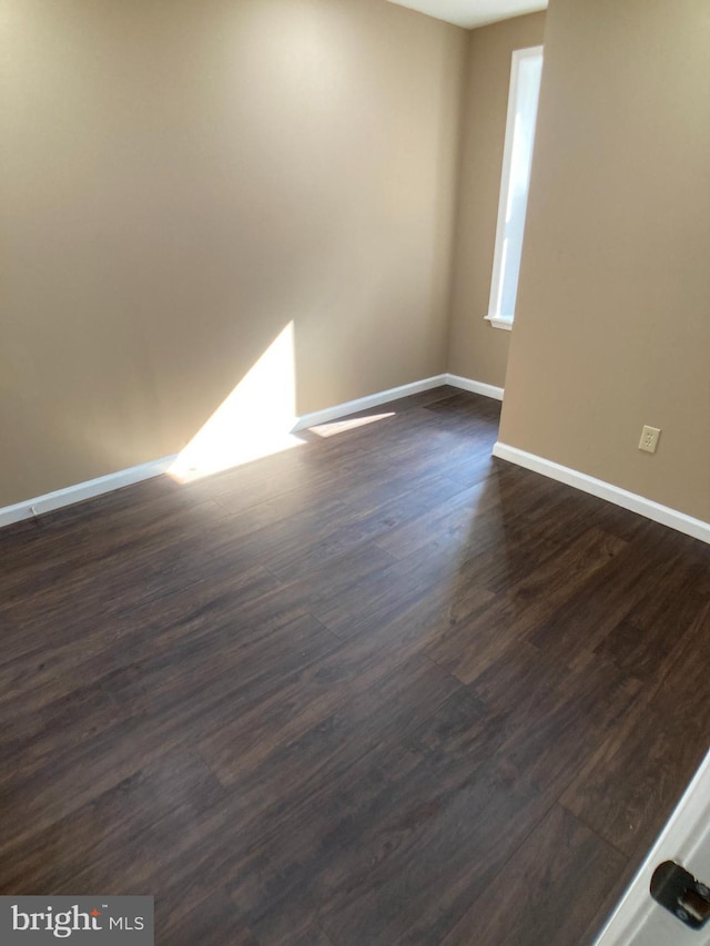 empty room with baseboards and dark wood-type flooring