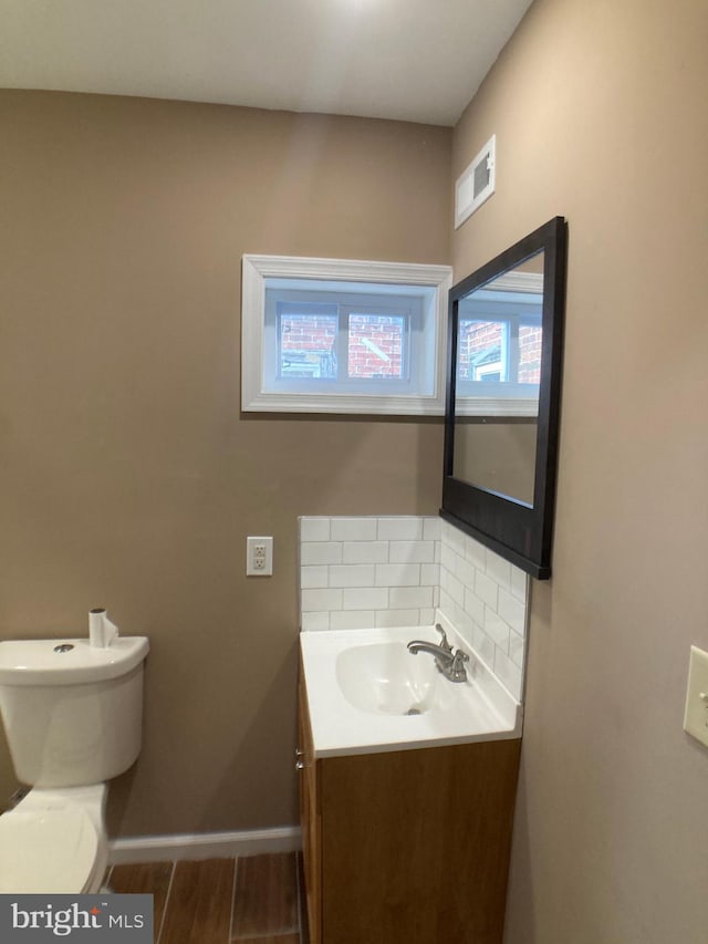 bathroom with baseboards, visible vents, wood finished floors, vanity, and backsplash