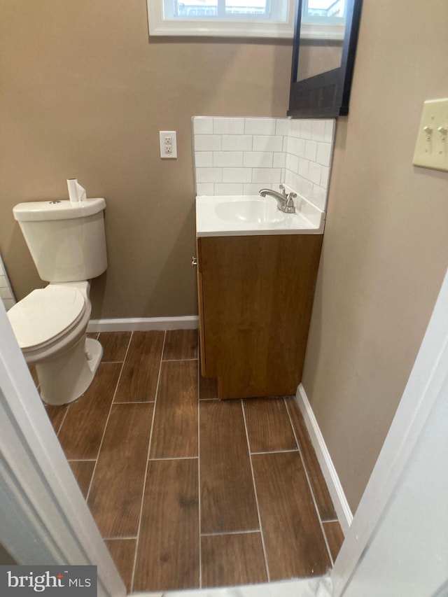 half bathroom featuring wood finish floors, baseboards, vanity, and toilet