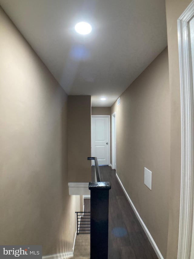 corridor featuring dark wood-style flooring, baseboards, visible vents, and an upstairs landing