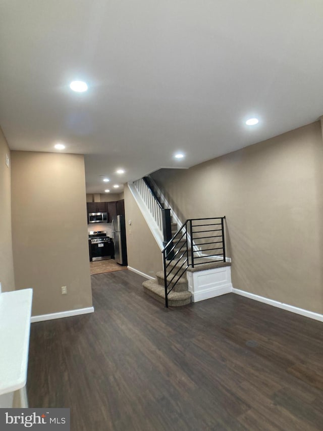 basement featuring recessed lighting, stairway, dark wood-type flooring, freestanding refrigerator, and baseboards