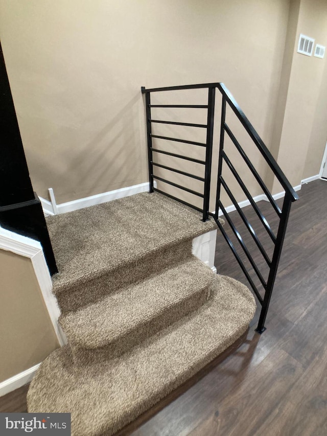 stairway featuring visible vents, baseboards, and wood finished floors