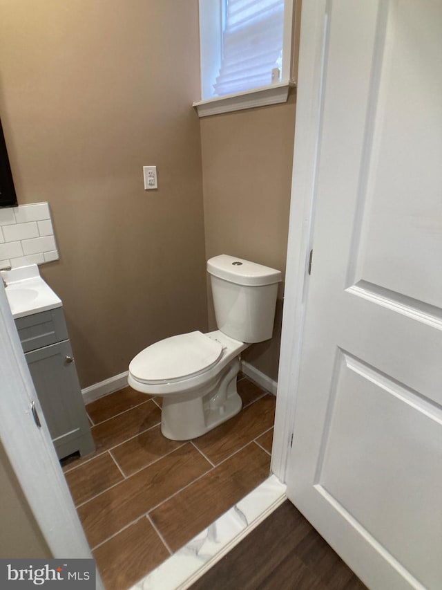 half bathroom featuring toilet, wood tiled floor, baseboards, and vanity