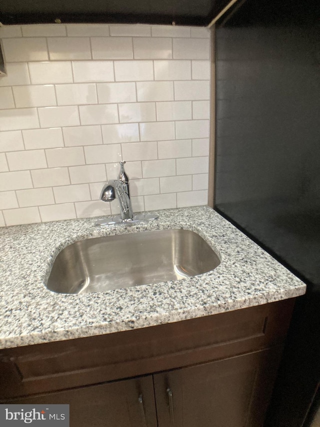 room details with tasteful backsplash, light stone counters, dark brown cabinets, and a sink