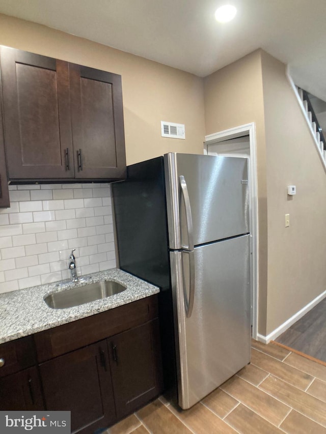 kitchen featuring visible vents, freestanding refrigerator, light stone countertops, dark brown cabinets, and a sink