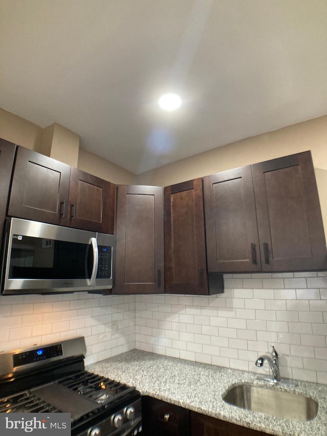 kitchen featuring dark brown cabinetry, light stone countertops, a sink, appliances with stainless steel finishes, and decorative backsplash