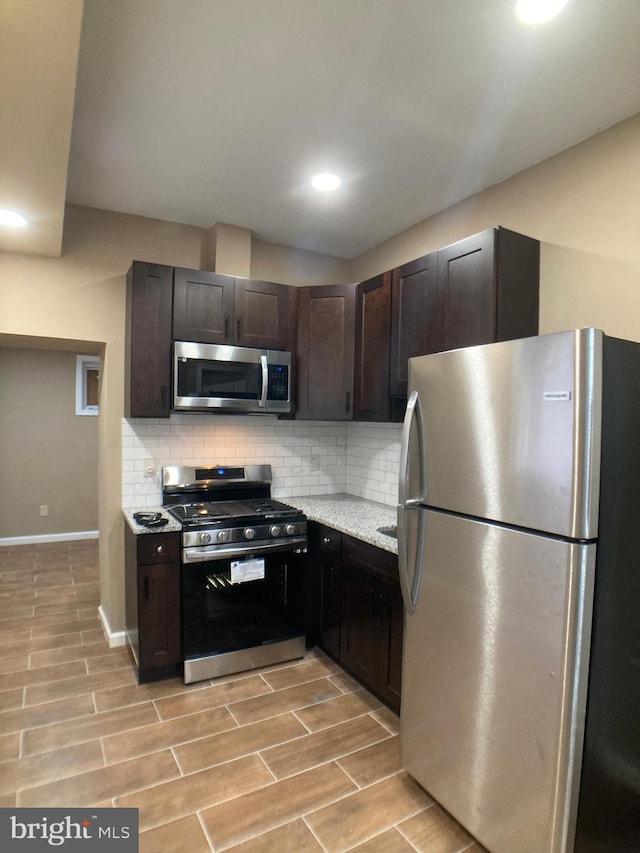 kitchen with stainless steel appliances, tasteful backsplash, wood tiled floor, dark brown cabinetry, and light stone countertops