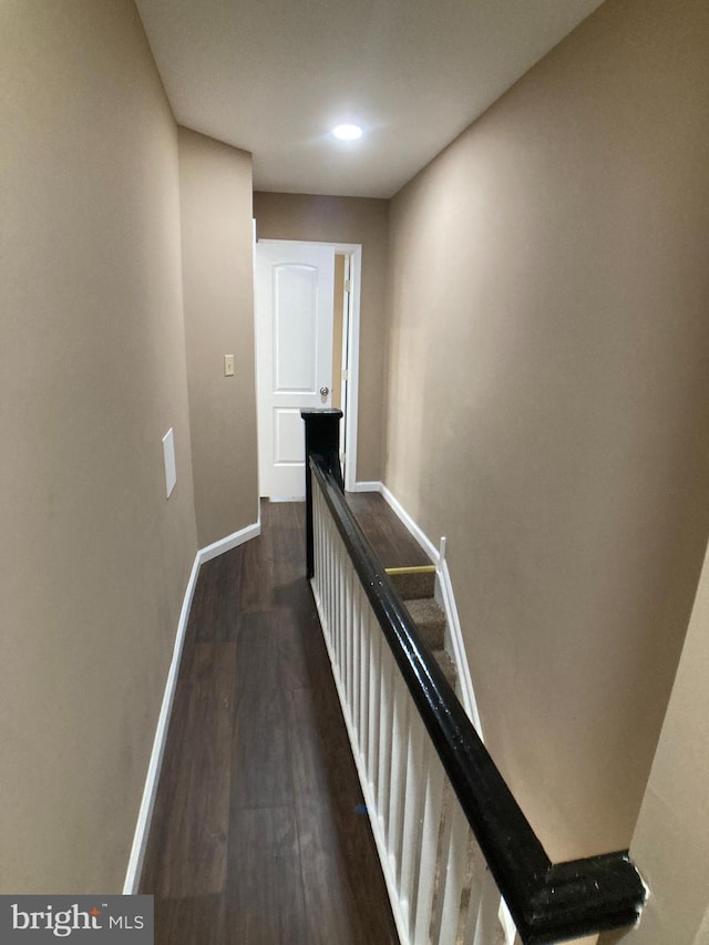 corridor with baseboards, dark wood finished floors, and an upstairs landing