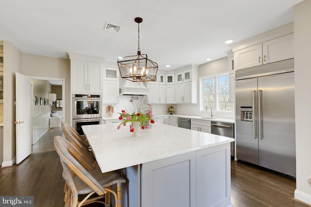 kitchen featuring visible vents, a kitchen island, glass insert cabinets, stainless steel appliances, and a sink