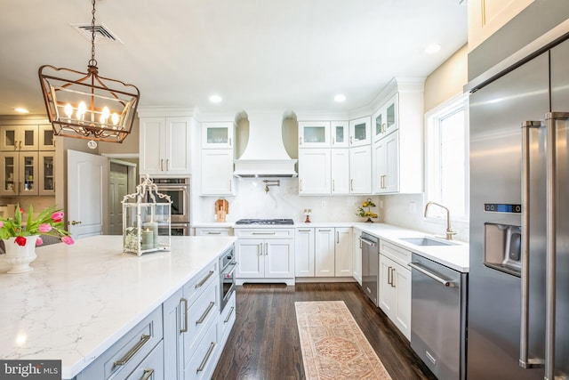 kitchen featuring decorative light fixtures, custom exhaust hood, stainless steel appliances, white cabinetry, and a sink