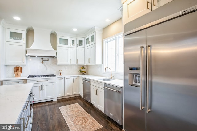 kitchen featuring white cabinets, glass insert cabinets, appliances with stainless steel finishes, premium range hood, and a sink