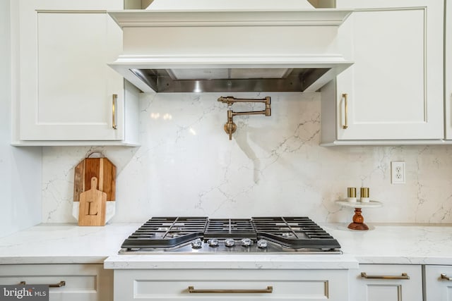 kitchen with stainless steel gas cooktop, decorative backsplash, white cabinetry, light stone countertops, and premium range hood