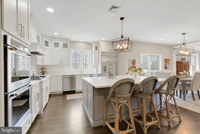 kitchen with stainless steel appliances, a kitchen island, visible vents, white cabinets, and light countertops