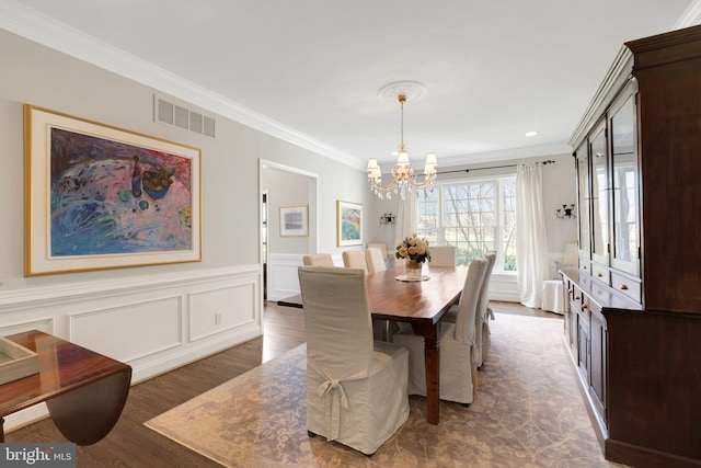 dining room featuring dark wood-type flooring, a decorative wall, visible vents, and crown molding