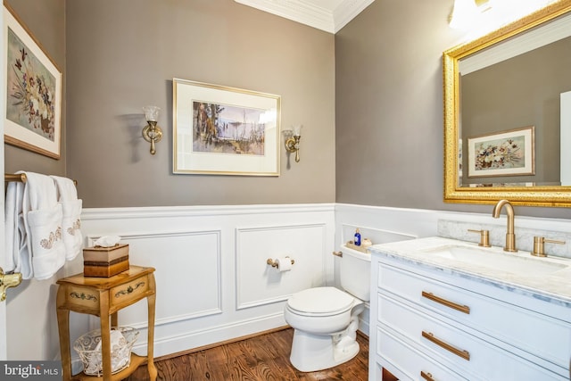 half bathroom featuring toilet, ornamental molding, wainscoting, vanity, and wood finished floors