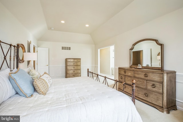 bedroom with a wainscoted wall, lofted ceiling, light colored carpet, visible vents, and a decorative wall