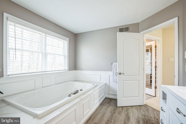 full bath with a wainscoted wall, visible vents, vanity, wood finished floors, and a bath